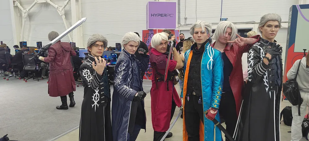 Группа людей в костюмах, возможно, на мероприятии или конвенте, с мечами и различными цветами одежды.