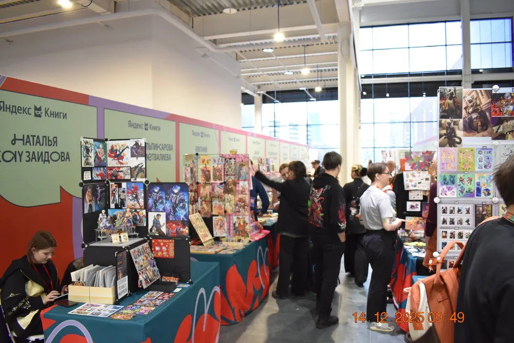 Изображение выставки или ярмарки, на которой люди находятся возле стендов с книгами и товарами, в том числе комиксами и рисунками.