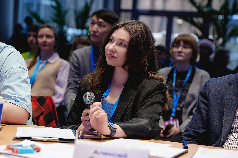 На изображении группа людей, одна из которых держит микрофон. Внимание на выступление или обсуждение.