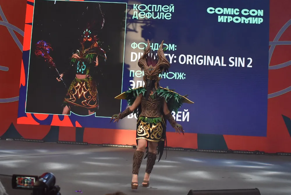 Изображение человека в костюме на мероприятии Comic Con, фон с текстом о игре Divinity: Original Sin 2.