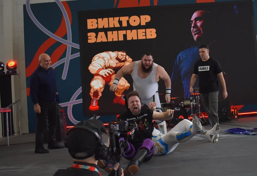 Изображение людей на спортивном мероприятии, видно участников и зрителей, на заднем плане баннер с именем \