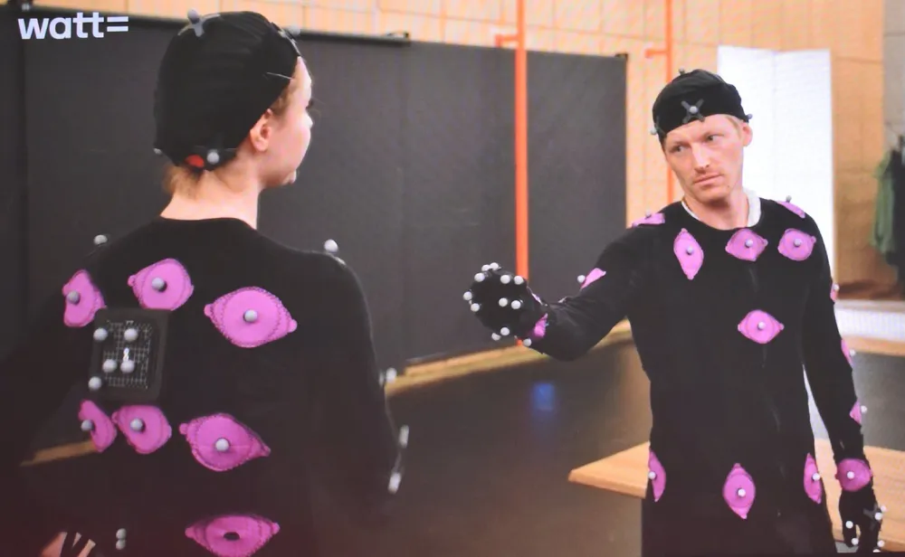 Изображение двух человек в костюмах для захвата движения, вероятно, в студии или на площадке для съёмок.