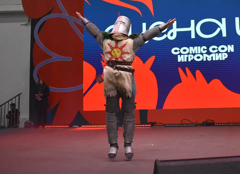 Человек в костюме рыцаря на мероприятии, фон с надписью "Comic Con".