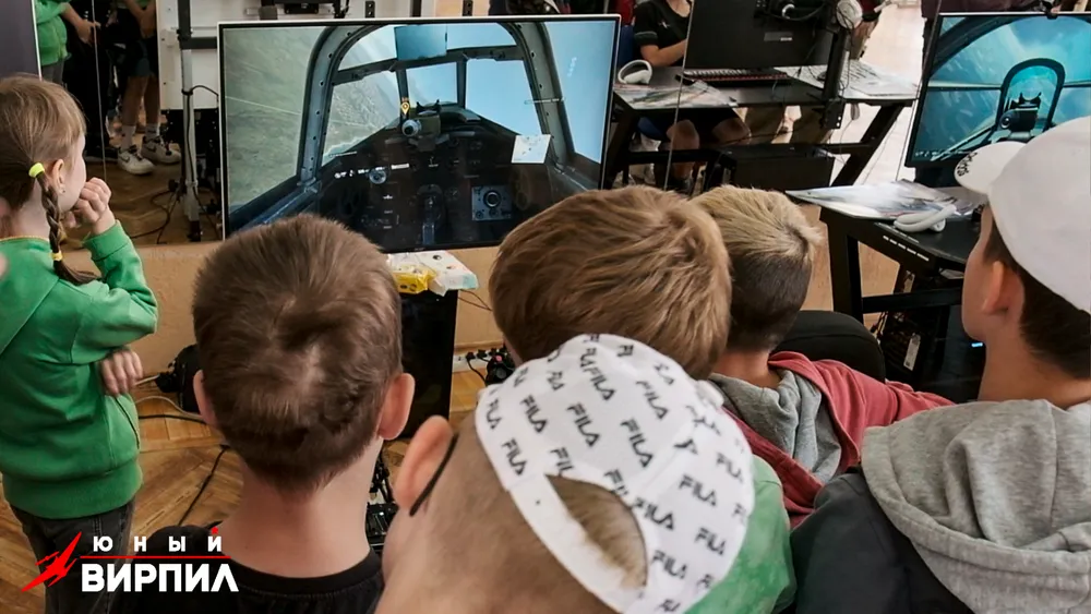 Группа детей наблюдает за игрой на большом экране. Видны элементы симулятора полета.