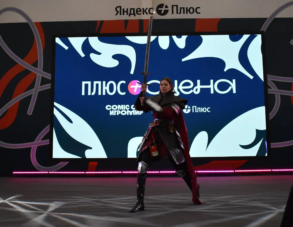 Изображение человека в костюме с мечом на фоне экрана с логотипом Яндекс Плюс.