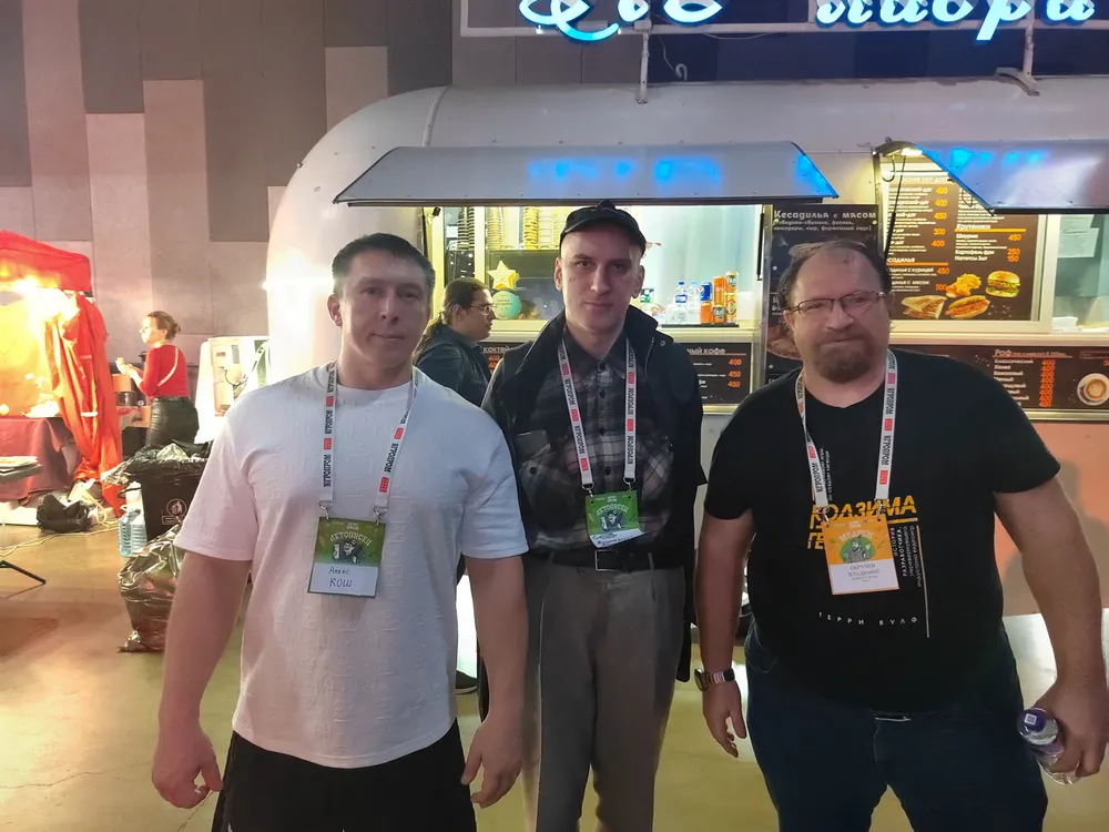 Трое мужчин на выставке или мероприятии, стоят рядом у фудкорта.