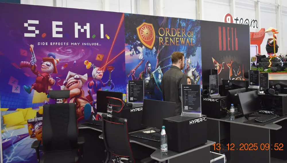 Изображение игрового стенда с компьютерными игровыми системами и рекламными плакатами игр.