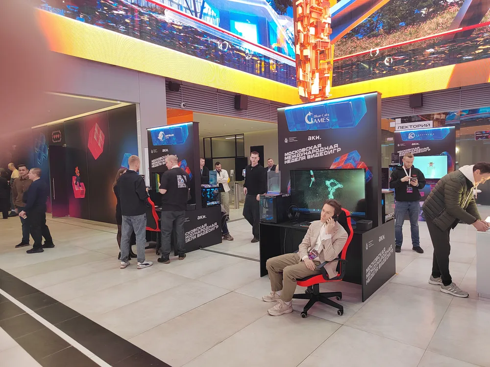 Изображение людей на выставке или мероприятии, люди взаимодействуют с выставочными стендами и играми.