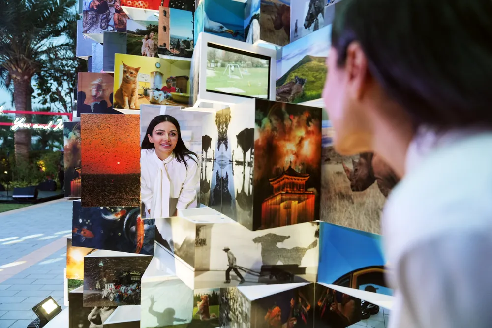 Изображение женщины, рассматривающей фотографии на стенде. Визуальные элементы включают различные изображения и людей.