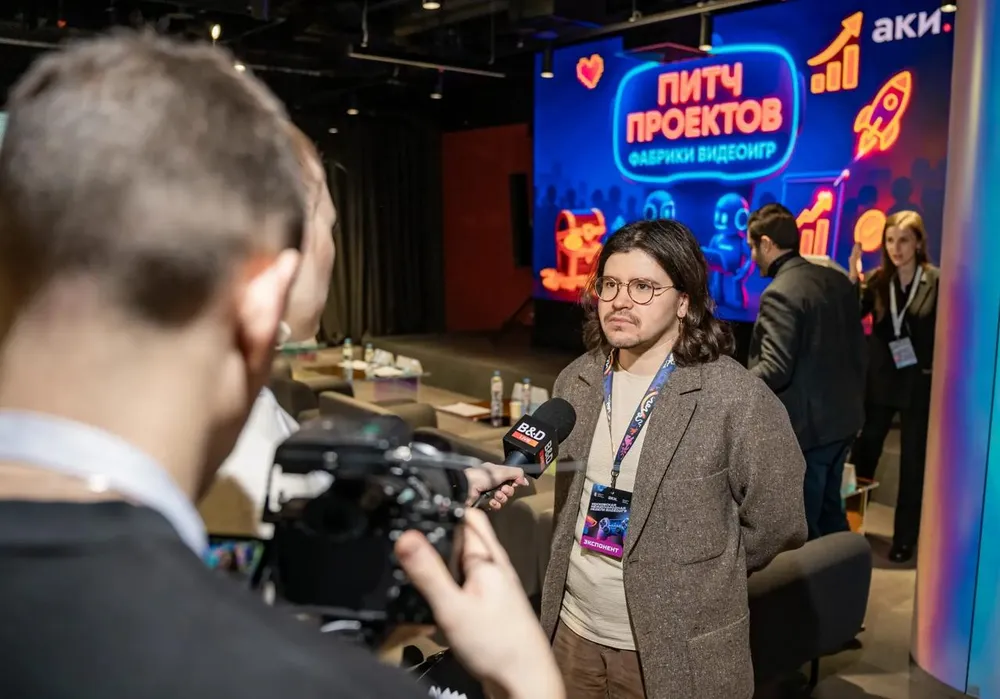 Изображение человека, проходящего интервью на мероприятии. На заднем плане виден баннер с текстом о пичах проектов.