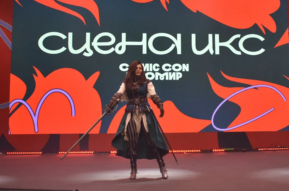 Изображение человека в костюме на сцене, с фоном, содержащим текст и графику.