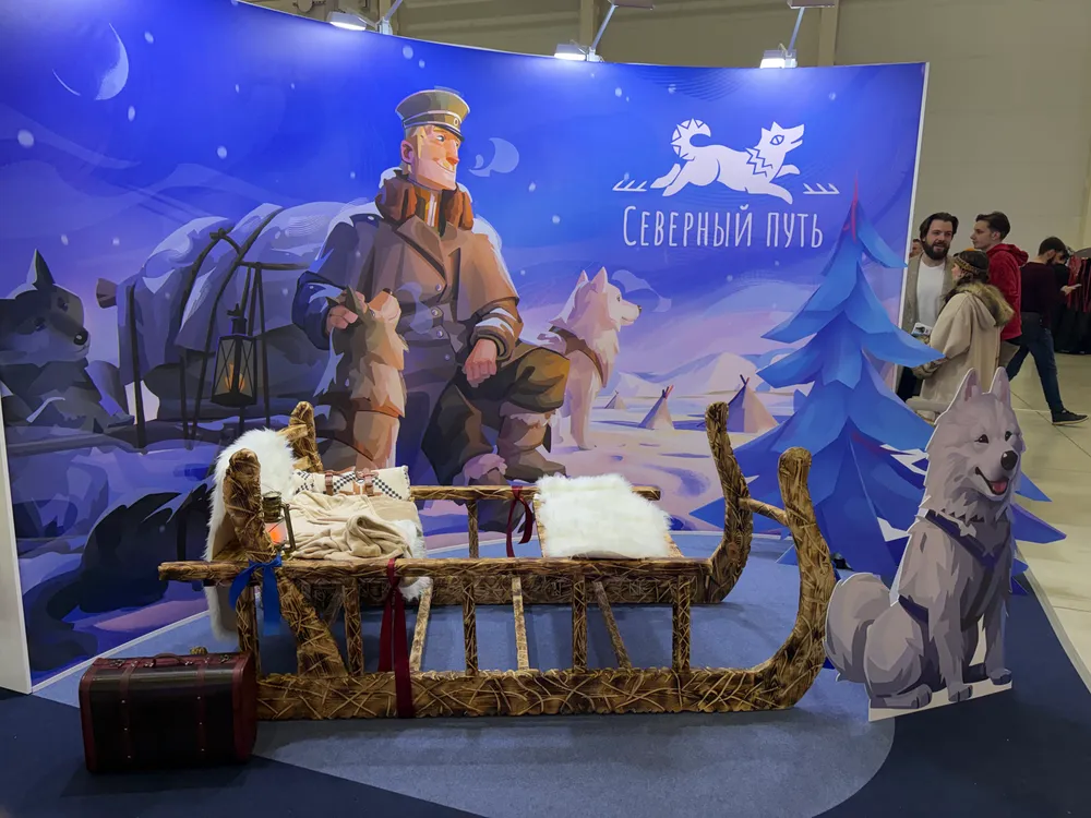 Изображение стенда с зимним пейзажем, персонажем в военной форме, собаками и санями. На заднем плане написано \