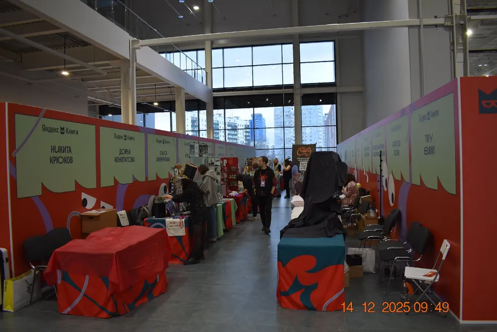 Изображение выставочного зала с рядами столов и стендами. Люди на мероприятии.