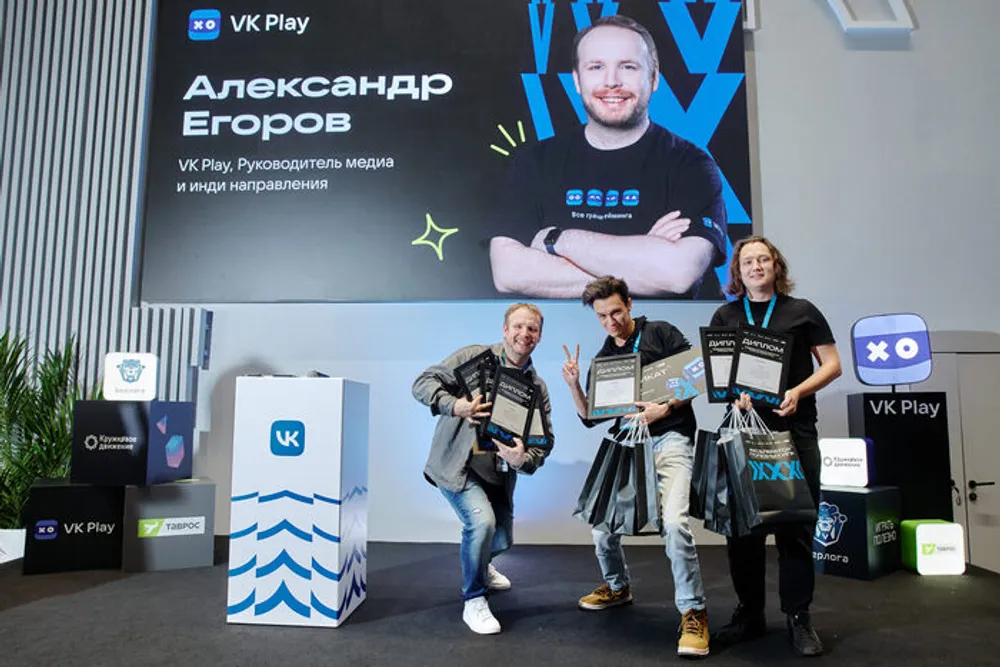 На изображении представлены люди, участвующие в мероприятии, с наградами и призами. Фон включает в себя логотипы и оформление, связанное с VK Play.