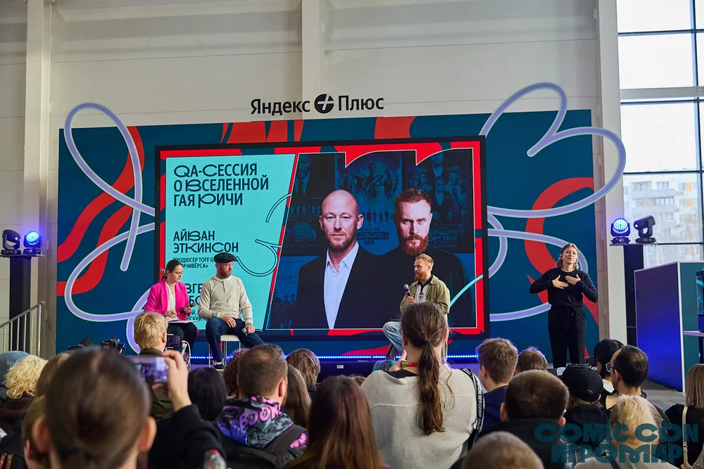 Мероприятие с участием людей на сцене, аудитория слушает, присутствуют участники и зрители.