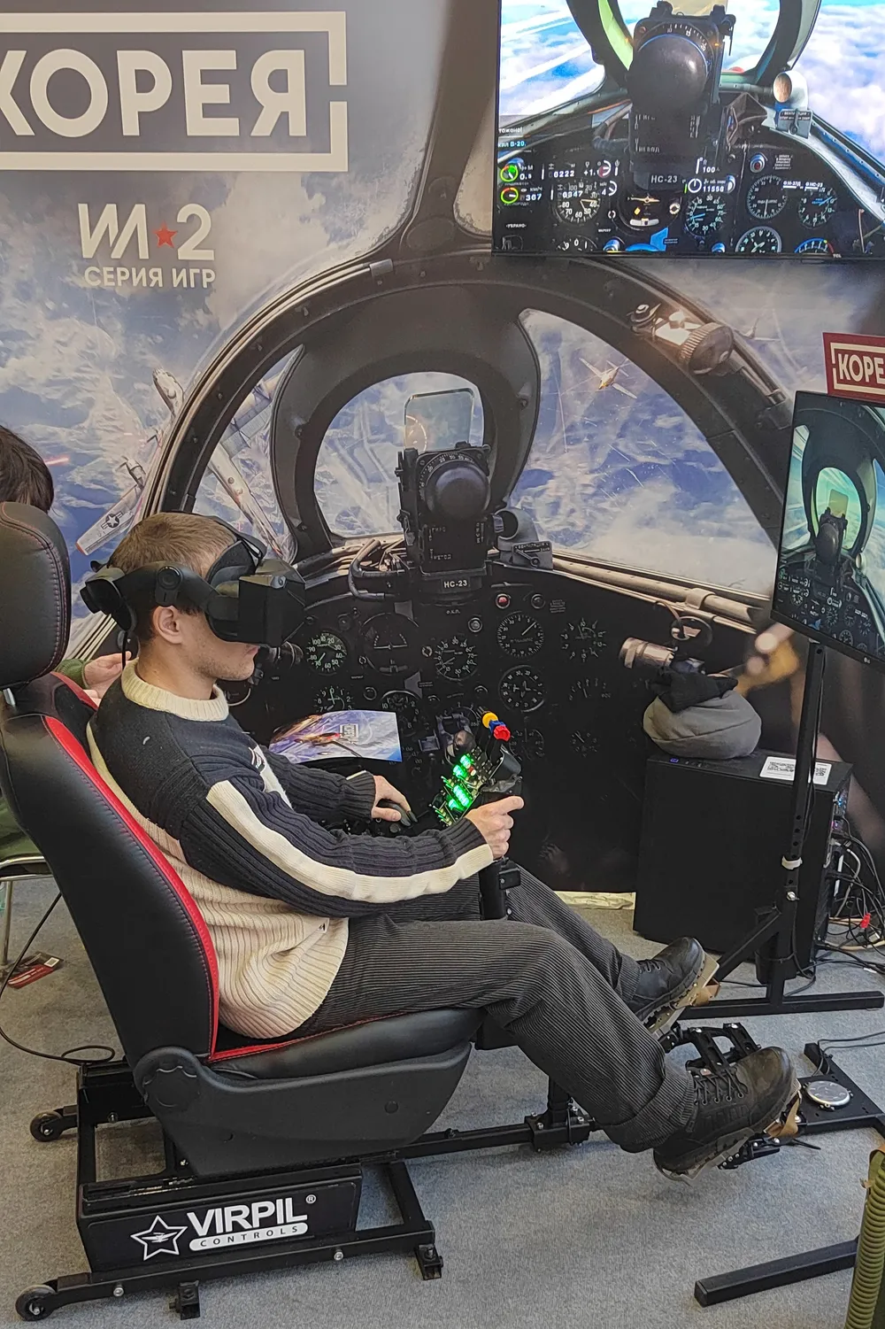 Изображение человека в виртуальной реальности, сидящего в игровом кресле с контроллерами в руках, на фоне авиационной тематики.
