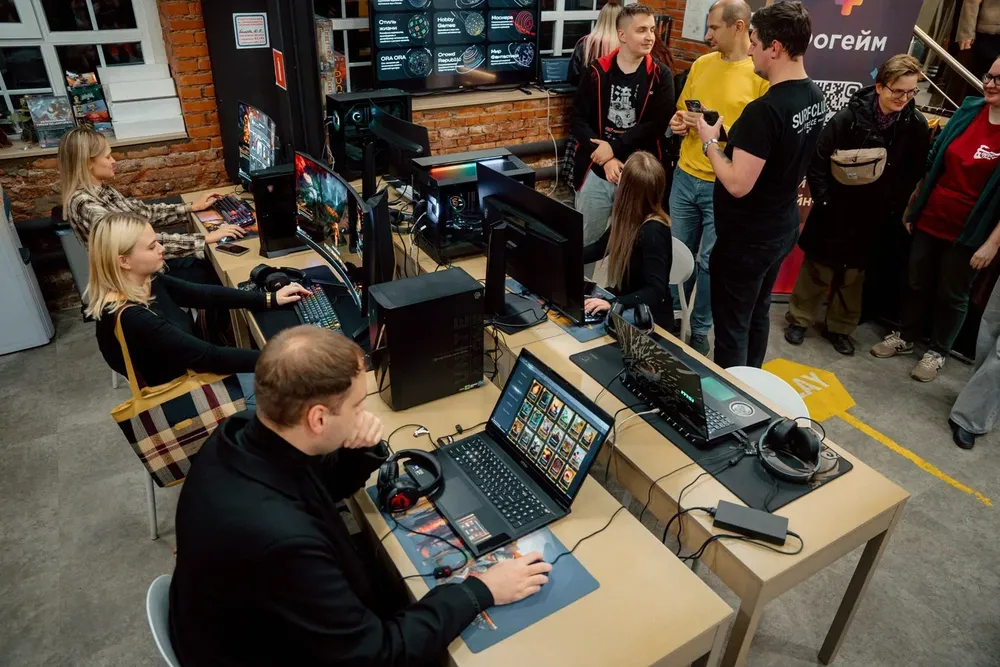 Группа людей за компьютерами в помещении, занимаются играми или работой. Наличие нескольких участников, некоторые из них общаются.