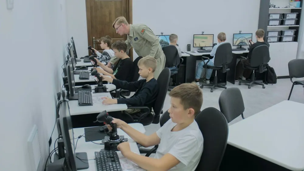 Изображение учащихся за компьютерами в классе, один взрослый, обучающий детей.