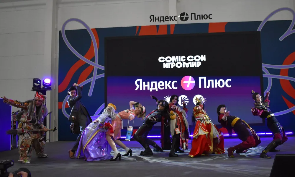 На изображении группа людей в костюмах на сцене мероприятия, название \