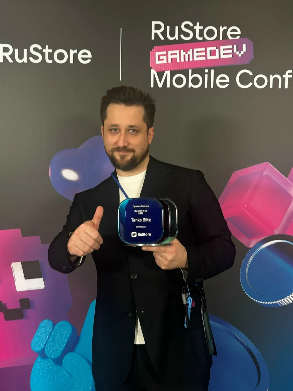 На изображении человек с наградой на фоне стенда RuStore GameDev Mobile Conference.