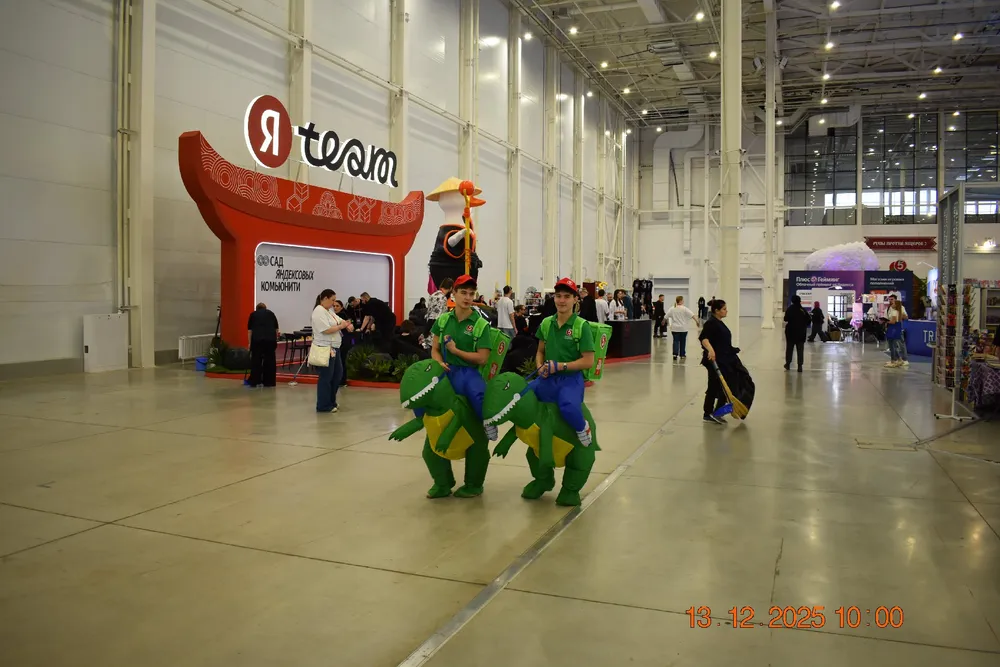 Изображение представляет собой мероприятие в помещении, где люди в костюмах животных. Видно стенд с логотипом \