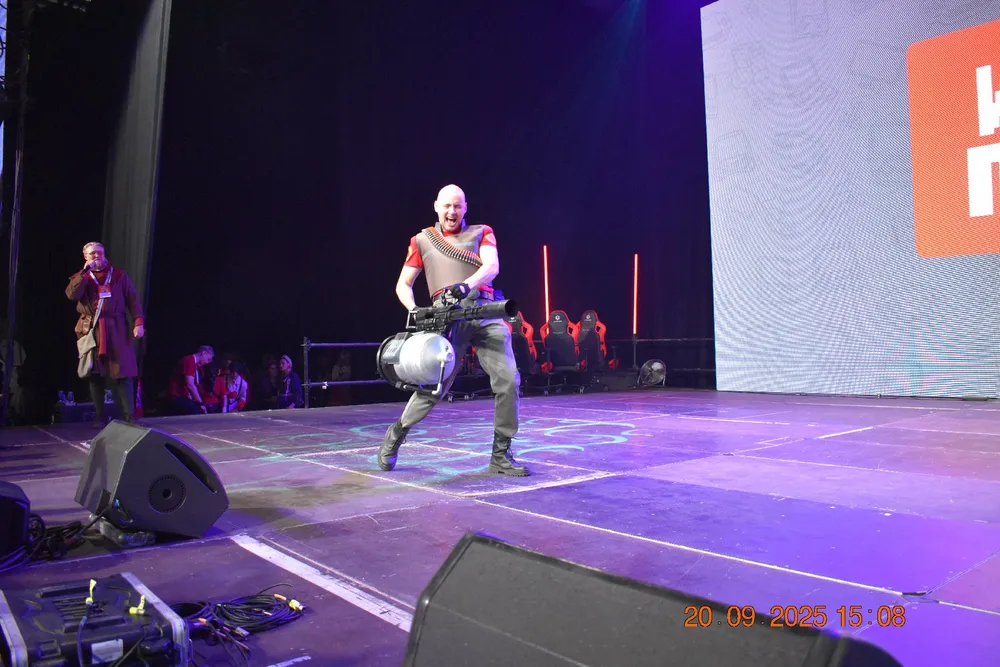 Изображение человека на сцене, возможно, во время выступления или шоу. Он одет в костюм и держит некий предмет в руках.