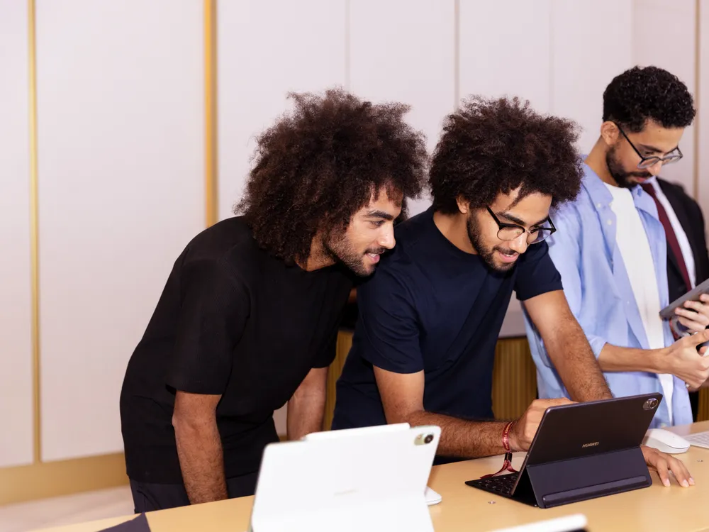 На изображении группа людей, работающих с планшетом и ноутбуком в офисной обстановке.