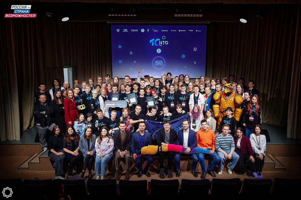 Группа людей на сцене, мероприятие, возможно, посвященное какой-либо тематике, с баннером на заднем плане.