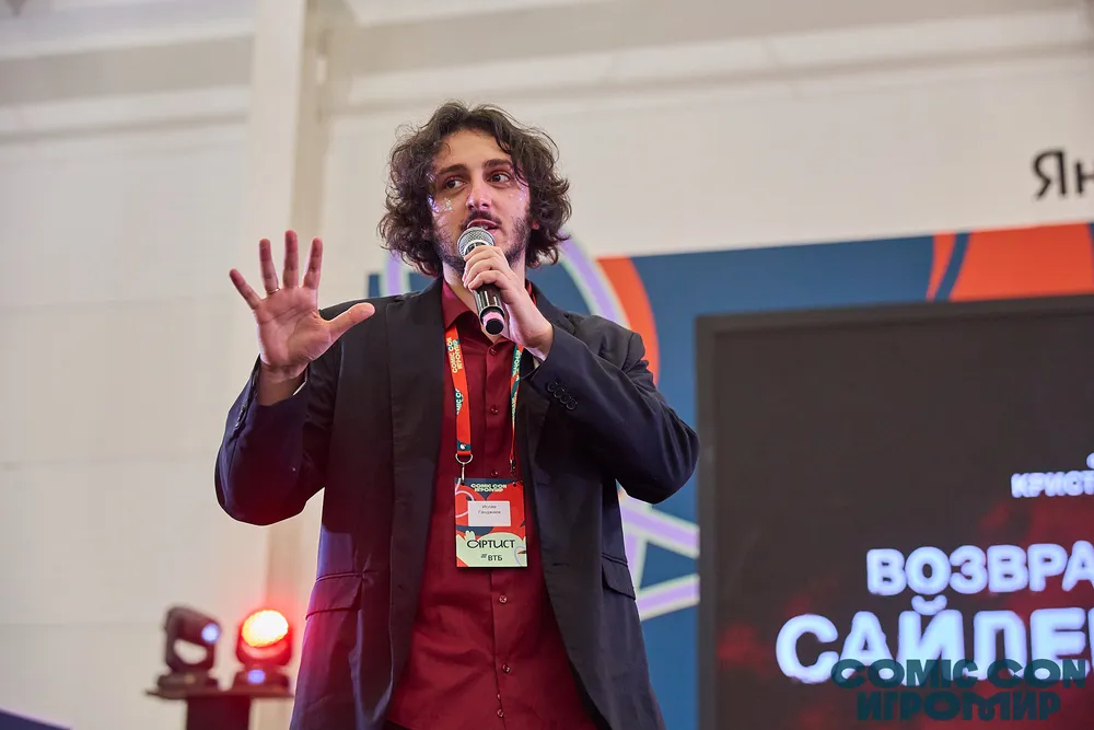 Человек на сцене с микрофоном, ведущий мероприятие или выступление.