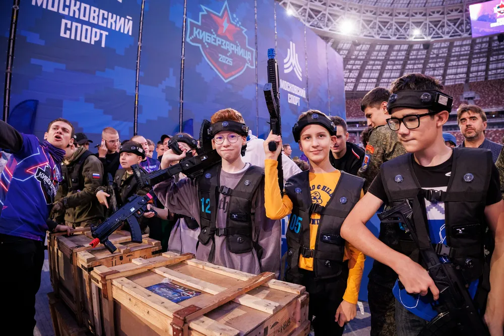 Группа детей и подростков на мероприятии, они держат игрушечные винтовки, в фоновом плане спортивная арена.