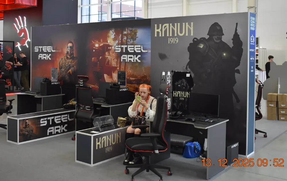 Изображение выставочного стенда с игровыми компьютерами и персонажем в костюме, обстановка выставки.