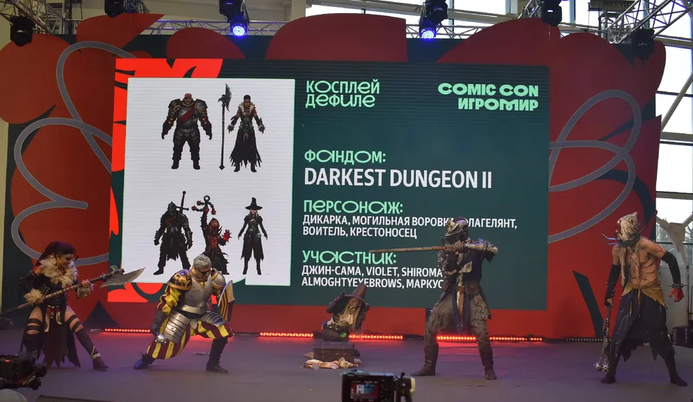 Изображение с косплеем персонажей из игры Darkest Dungeon II на мероприятии Comic Con. На сцене несколько участников в костюмах.