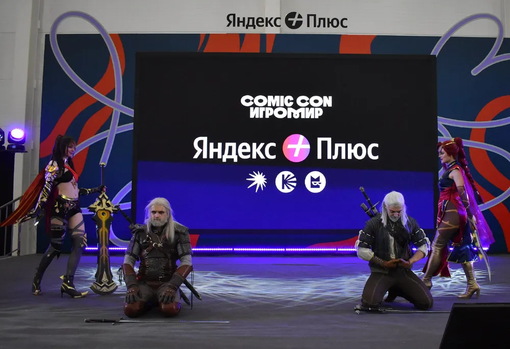 Косplay персонажей на мероприятии Comic Con, сцена с несколькими участниками, на фоне рекламный баннер.