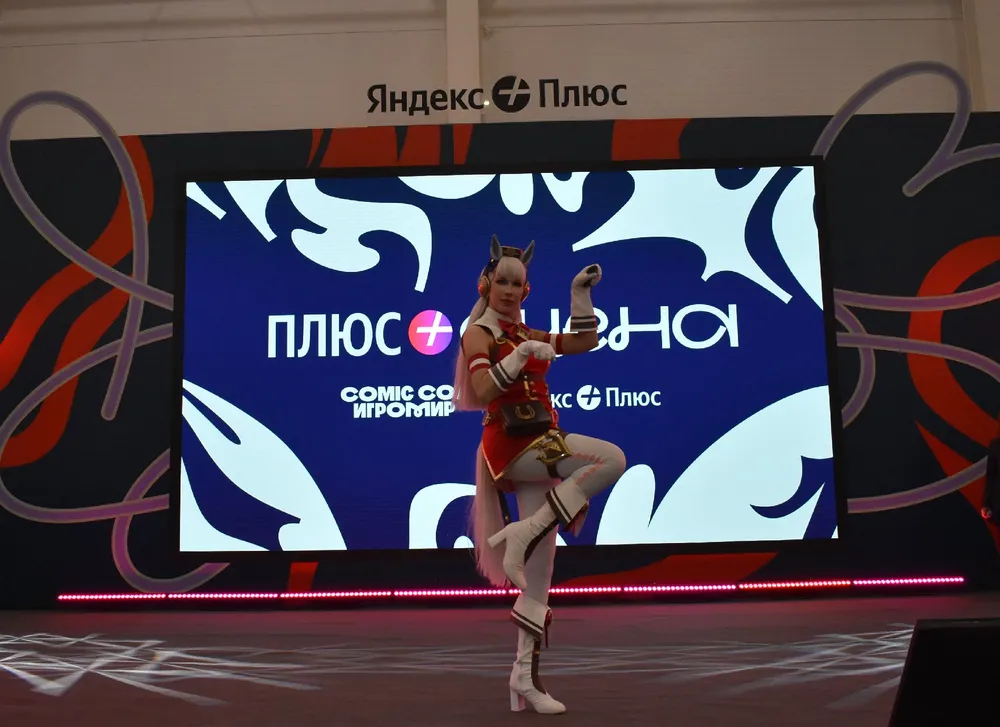 Изображение человека в костюме на сцене, с логотипом Яндекс Плюс на заднем плане.