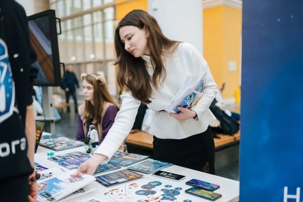 На картинке изображены два человека, один из которых рассматривает материалы на столе. Вокруг видно пространство с ярким освещением.