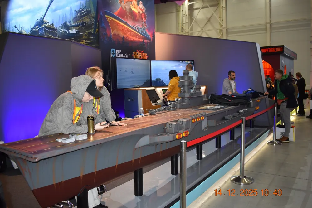 Изображение выставочного стенда с людьми, играющими в видеоигры, и моделями кораблей.