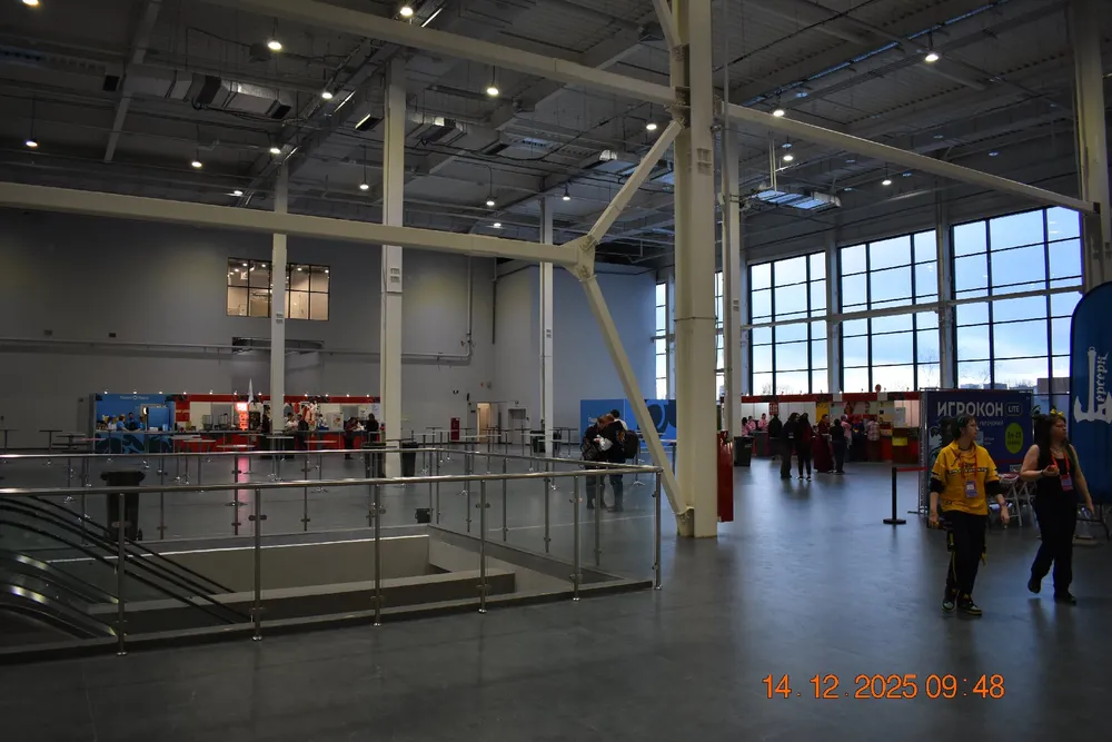 Интерьер большого помещения, вероятно, выставочный зал или торговый центр. Люди в фоновом режиме.