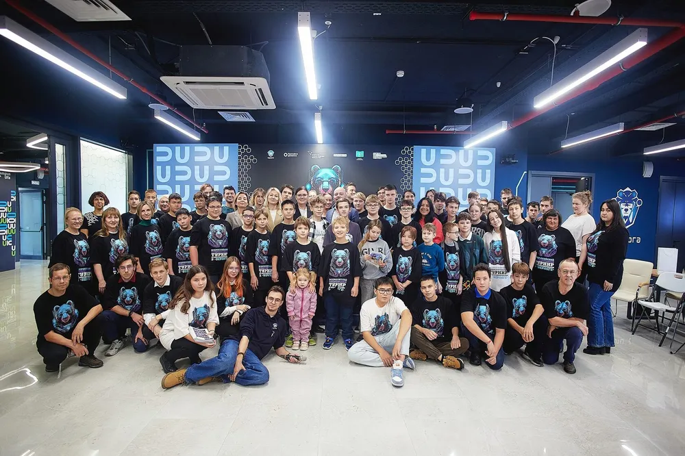 Группа людей на мероприятии, все в одинаковых футболках, интерьер помещения с неоновой подсветкой.