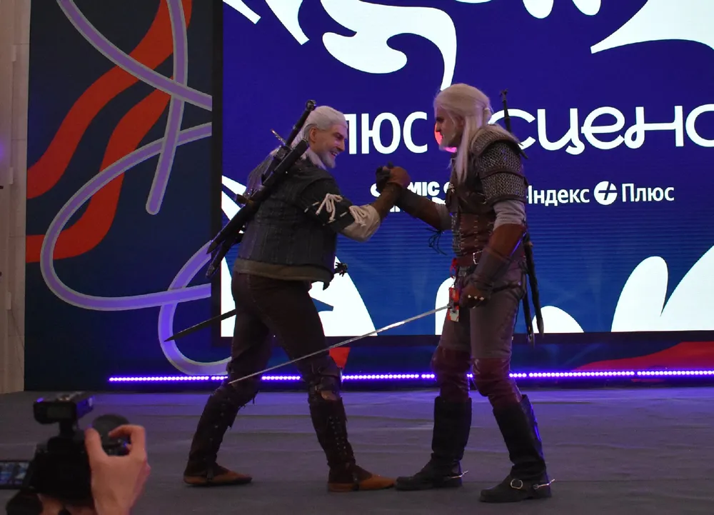 Два человека в костюмах, возможно, из игры или фильма, на сцене с фоном. Сцена представляет собой театральное представление.