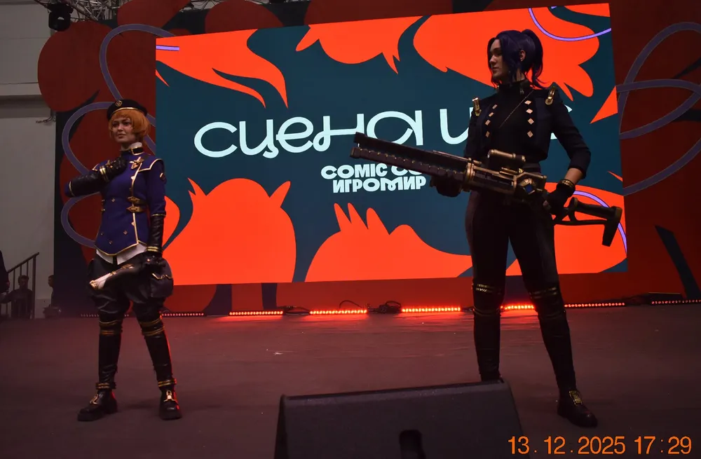 Два человека в костюмах на сцене, фон с графикой мероприятия.