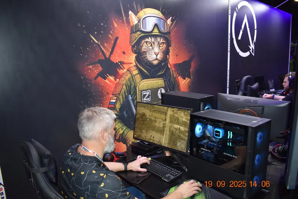 Изображение человека, сидящего за компьютером, на фоне графики с котом в военной форме.