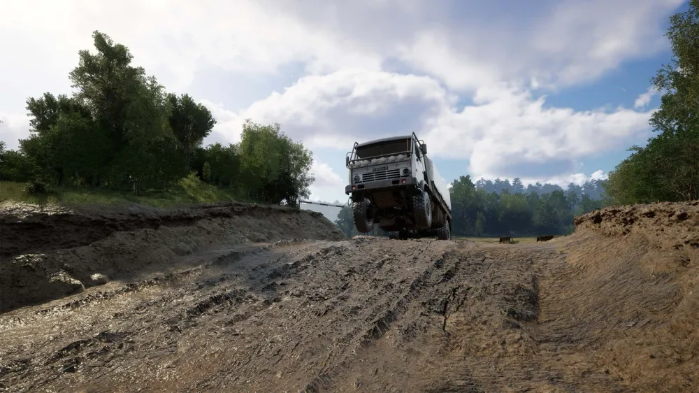 На изображении представлен грузовик, перемещающийся по неровной местности среди деревьев и облачного неба.