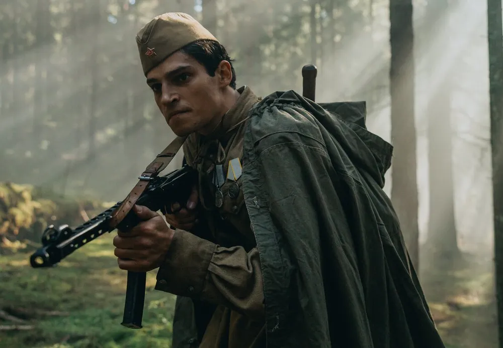 Мужчина в военной форме с оружием на фоне леса.