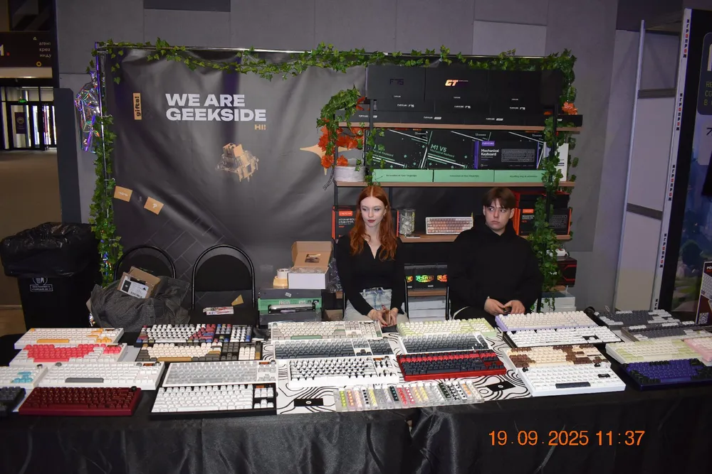 На изображении представлены два человека за столом с клавиатурами и оборудованием, на фоне баннер с надписью \