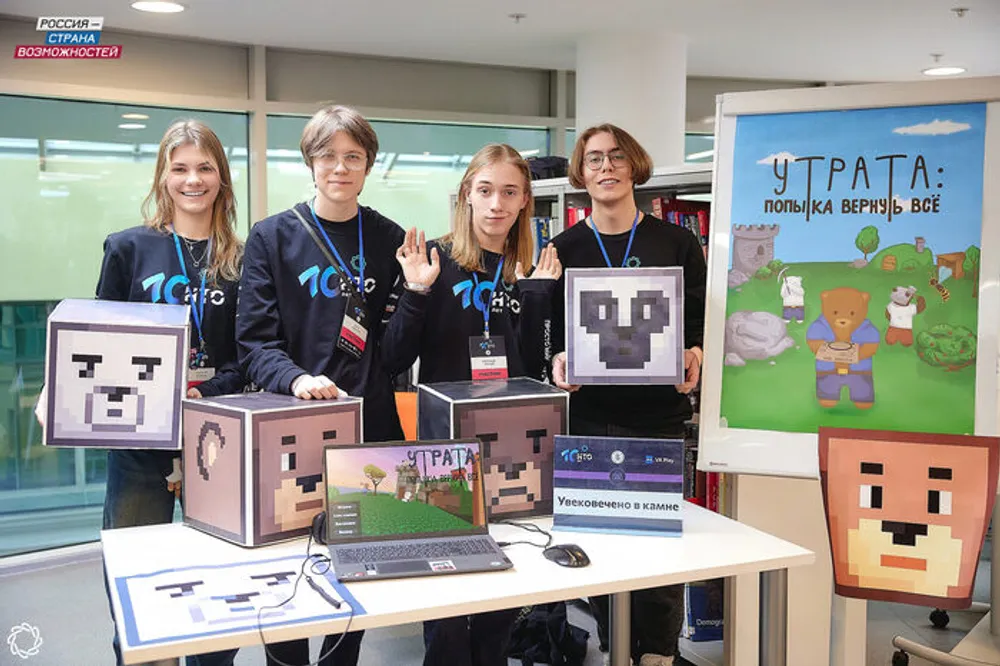 Группа людей на мероприятии, демонстрирующие различные предметы и компьютеры. На заднем плане виден баннер с надписью \