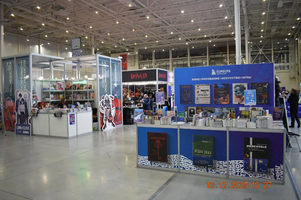 Изображение выставочного зала с выставочными стендами и книгами. На переднем плане стоит стенд с книгами и рекламными материалами.