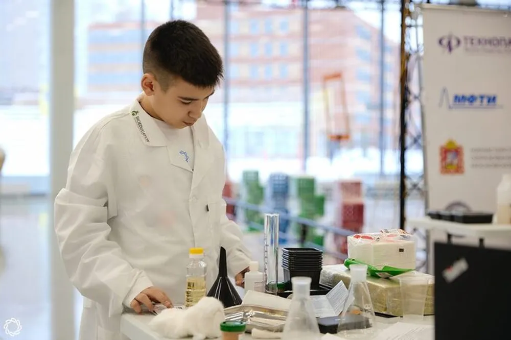 Мальчик в лабораторном халате работает с лабораторным оборудованием на столе.