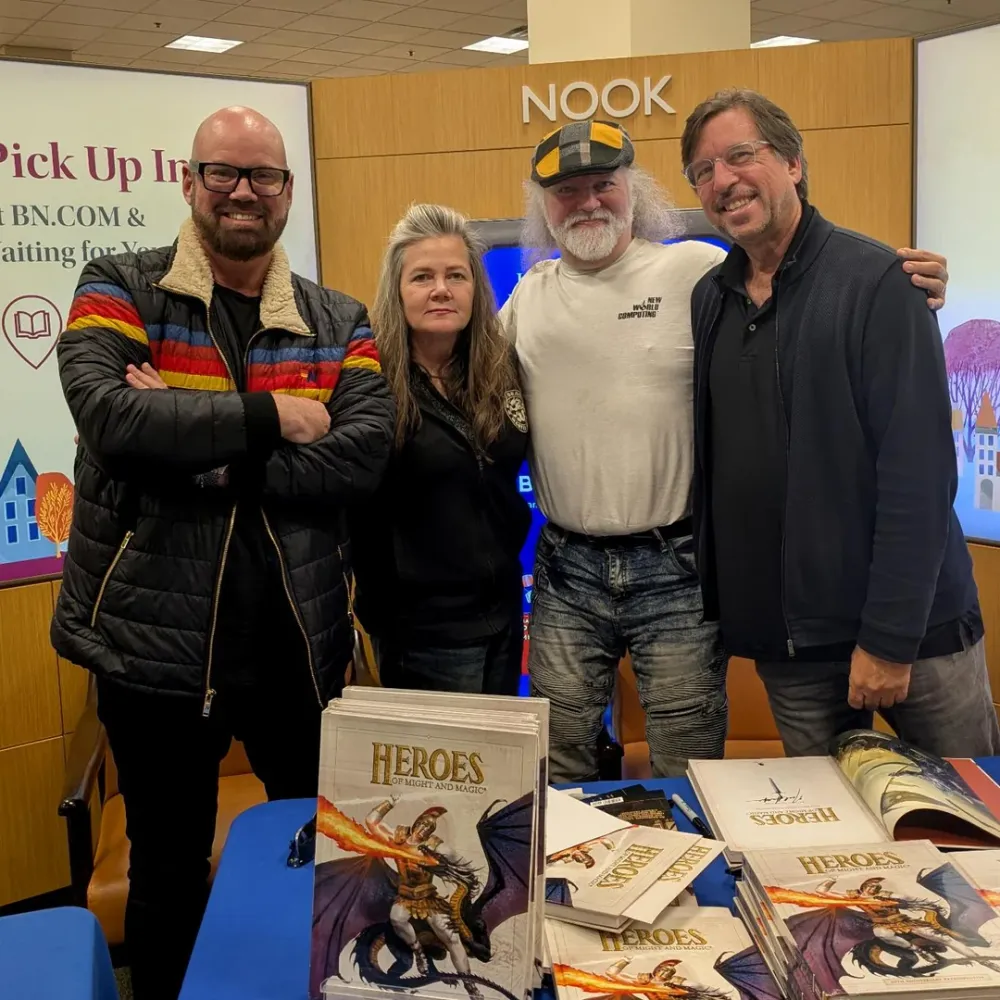 Четыре человека позируют вместе на фоне стенда с книгами. На столе лежат книги с названием \