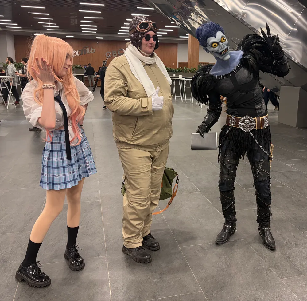 Трое людей в костюмах; один в школьной форме, другой в зимней одежде, третий в костюме персонажа с гримом.