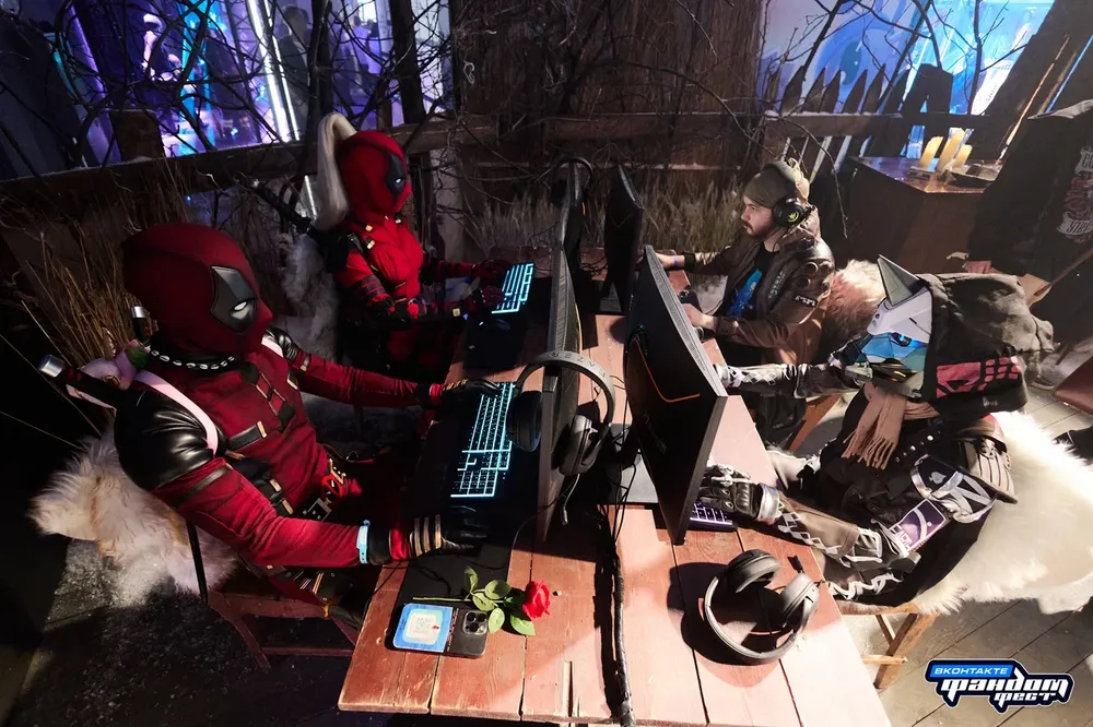 Четыре человека в костюмах, сидящие за компьютерами в игровой обстановке.